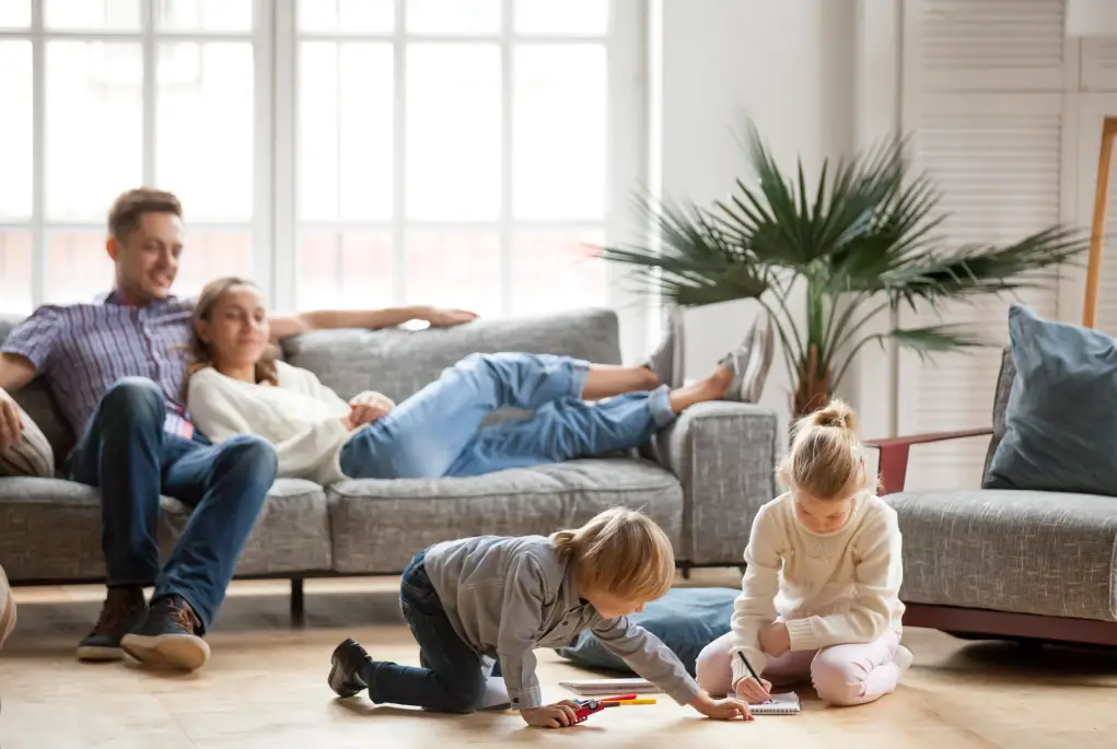 Happy parents sit back in their newly refinanced home while their two children draw in the foreground.