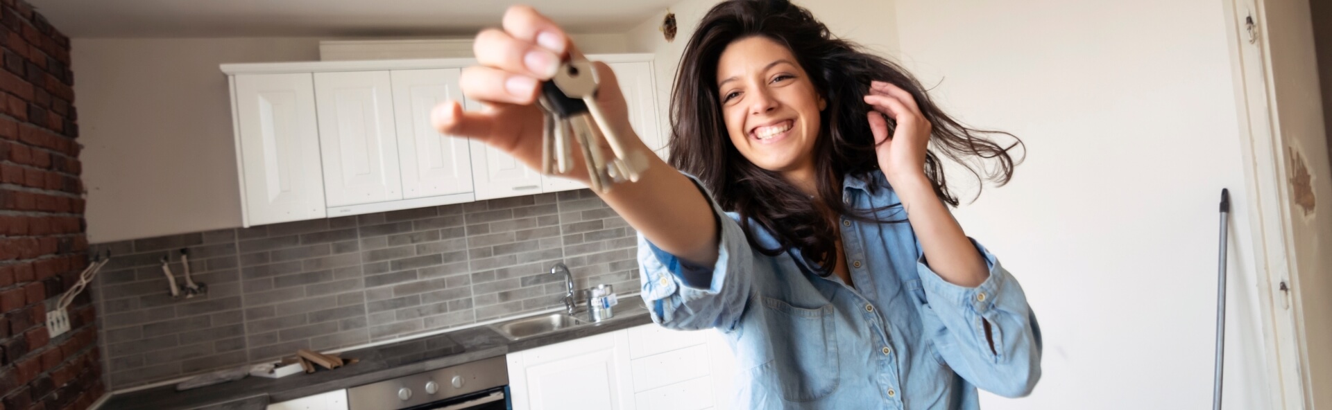 A young first home buyer proudly holding her house keys with a smile.