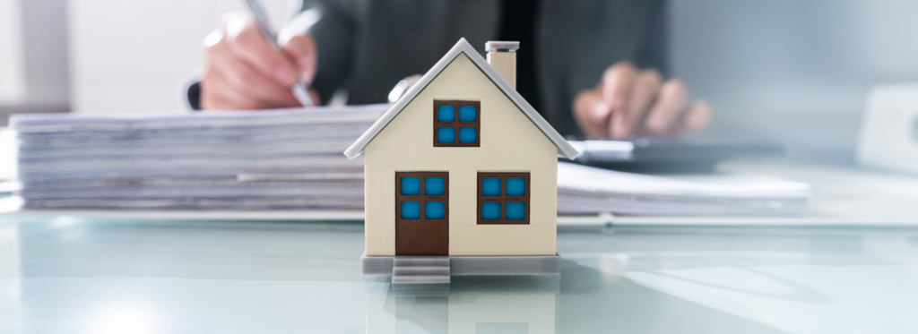 A small model house placed on an office desk whilst signing commercial property paperwork. 