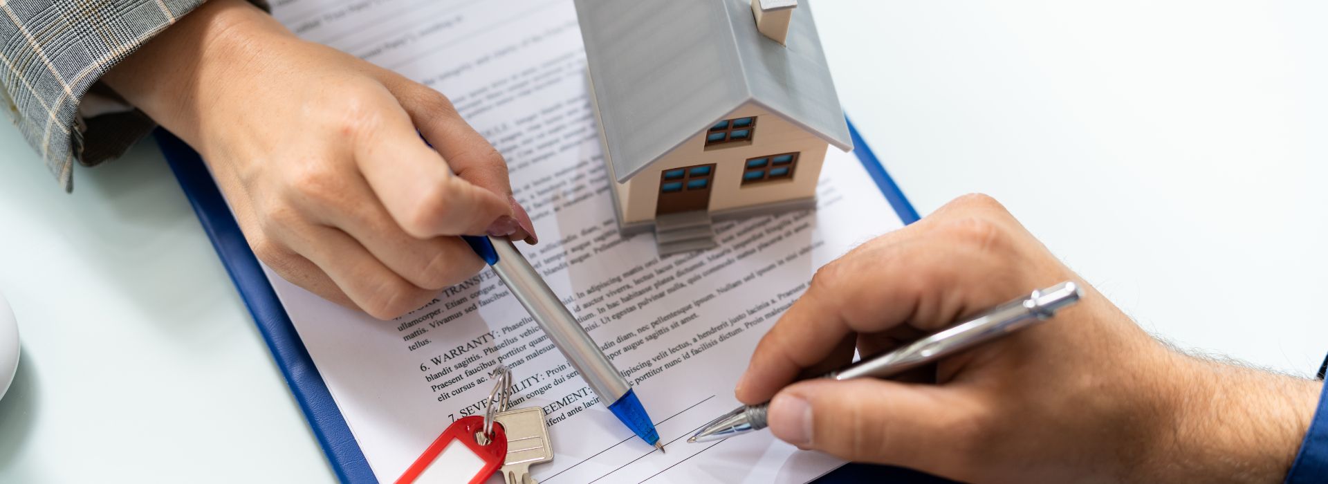 Hands signing property documents with house keys and a small wooden house model on a desk, representing the home buying and conveyancing process" This alt text describes the key visual elements that convey the context of property transactions and legal documentation, which would be relevant for your first home buyer conveyancing guide.