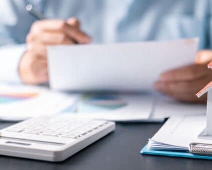 Financial workspace with house model and calculator. A person plans to save for their first home while renting, managing budgets.