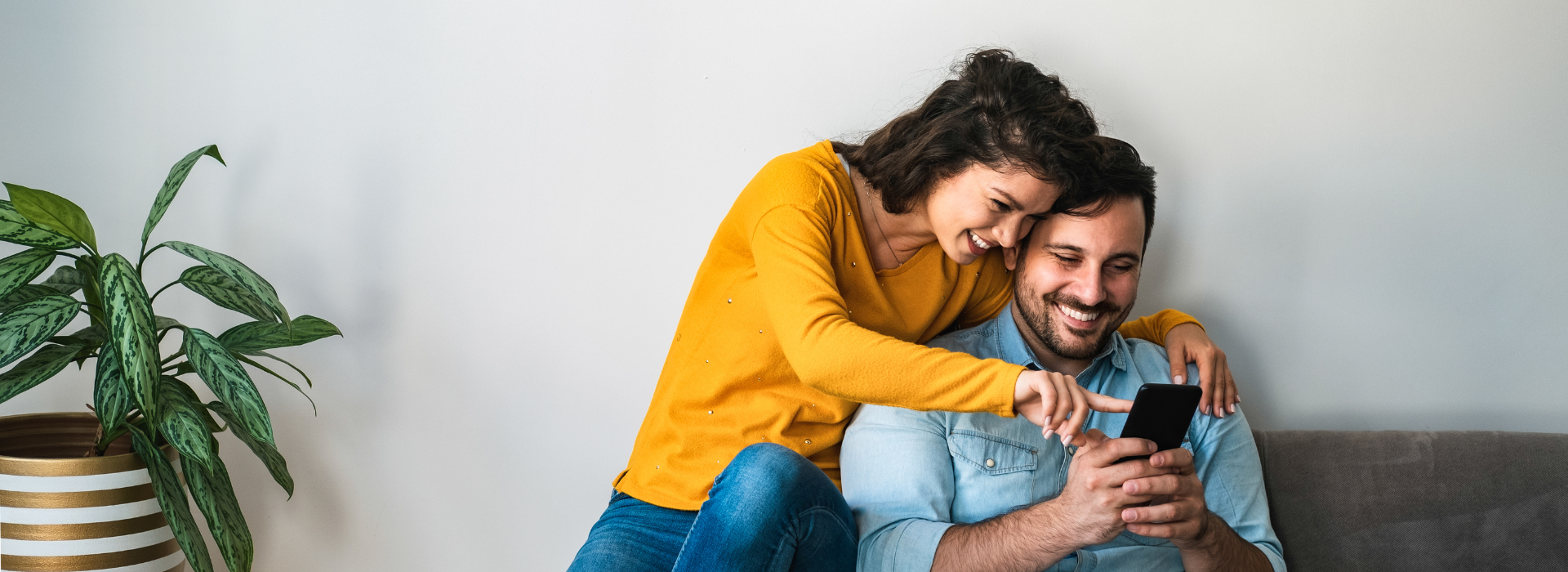 Happy couple on couch reviewing home loan options and discussing how family support through a guarantor can help secure their mortgage