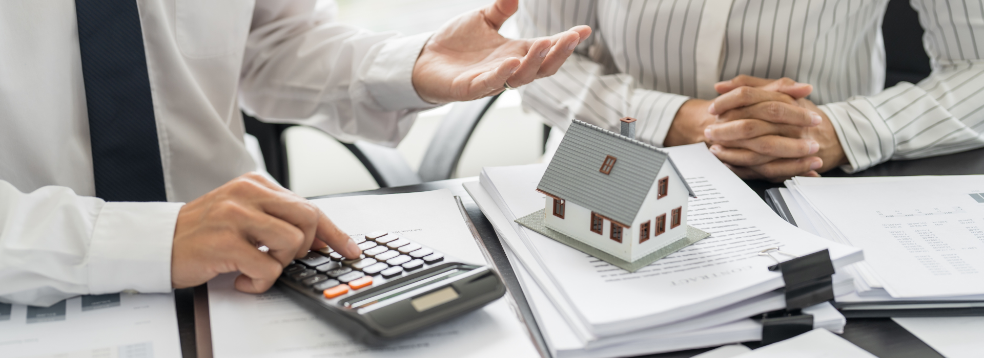 Lending Specialist calculating investment property costs with house model and loan documents for rentvesting