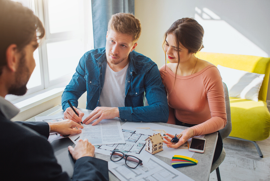 Couple meeting with their mortgage broker to sign guarantor home loan documents with house model on table