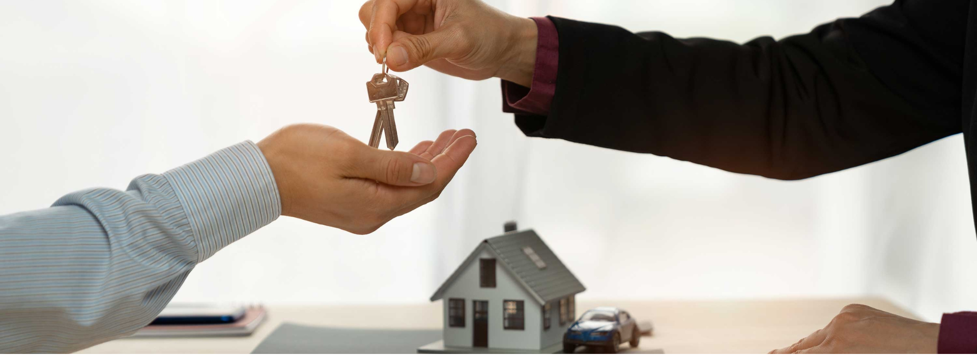 Hand passing house keys to first home buyer with model house in background